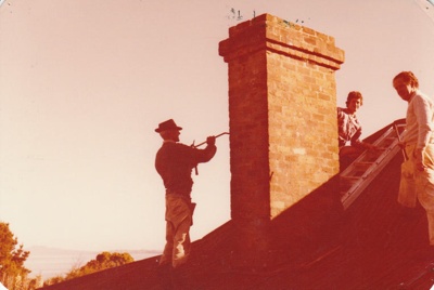 Men dismantiling the chimney on the roof of Eckford's homestead before removal to the Howick Historical Village. ; La Roche, Alan; 6 May 1978; P2021.09.17