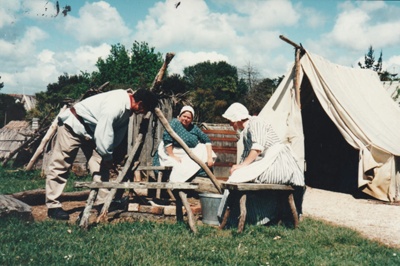 Debbie Benson and Prue Lees in costume cooking over the fire outside the tent on the green at Howick Historical Village.; La Roche, Alan; October 1996; P2021.88.03