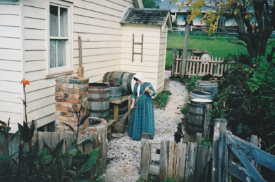 A volunteer in costume sweeping the path lined with beer barrels, outside the Howick Arms.; P2020.72.01