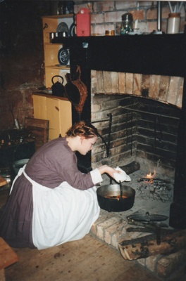 A woman, in costume, cooking in the fireplace in Sergeant Ford's cottage in Howick Historical Village.; La Roche, Alan; P2021.98.02