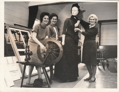 Alwyn Zellerman, Eileen Martensen and Dee Collings with a spinning wheel and mannequinat the 1964 exhibition of the Howick Historical Society in the Howick Town Hall.; October 1964; P2022.11.02