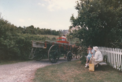 Christmas, past and present at Howick Historical Village, December 1987. Two women sitting n a bench oustide the Church watching a cart and driver passing.; Ashby, Frank; 12 December 1987; P2021.190.26