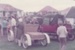 People looking at vintage cars in Howick Historical Village. Eckford's homestead and De Quincey'ss cottage are in the background.; La Roche, Alan; June 1982; P2021.10818