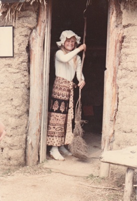 A Girl in costume sweeping the Sod Cottage, Howick Historical Village. ; 1986; P2020.45.11