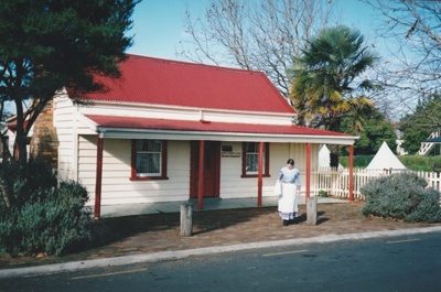 Brindle Cottage in the Howick Historical Village after the removal of the post box. A woman in costume is standing outside.; La Roche, Alan; P2021.42.01