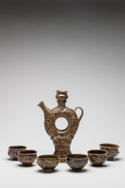 Wine decanter with six cups. Sculptured grape motif relief around body of decanter and cups. 