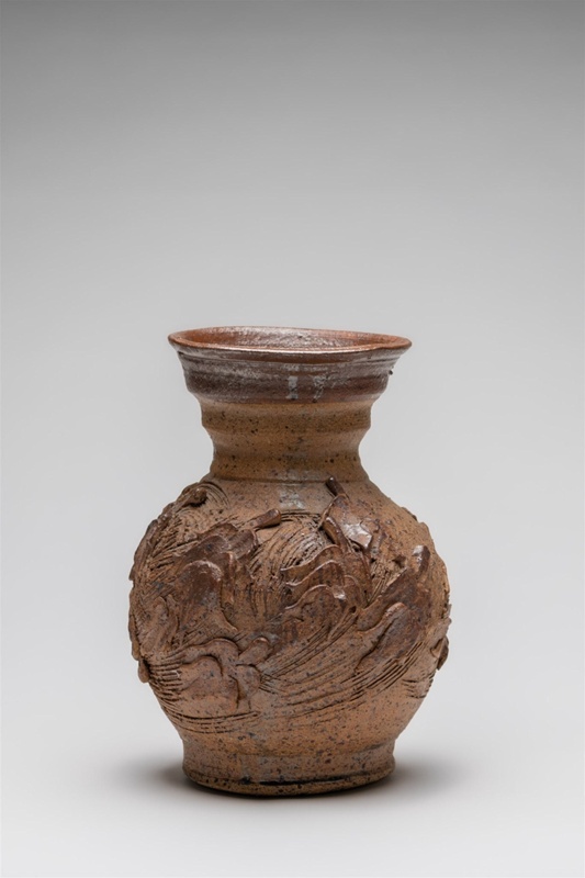 A highly textured terracotta vase with plant motif relief and diagonal linear incisions suggestive of windswept movement.  