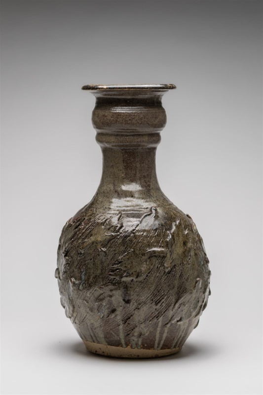 Heavy Floor vase with relief detailing of leaf motifs around the body. Incised vertical lines suggestive of movement, light grey-green glaze unevenly applied.