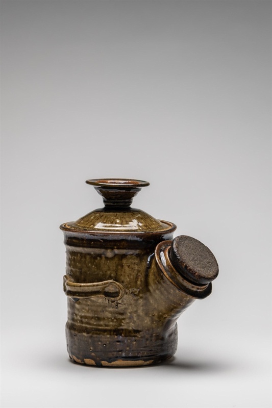 Large condiment jar with corked side lip two sculptured handles and prominent lid for filling the vessel. Hairline crazing in the light olive-green stain glaze.