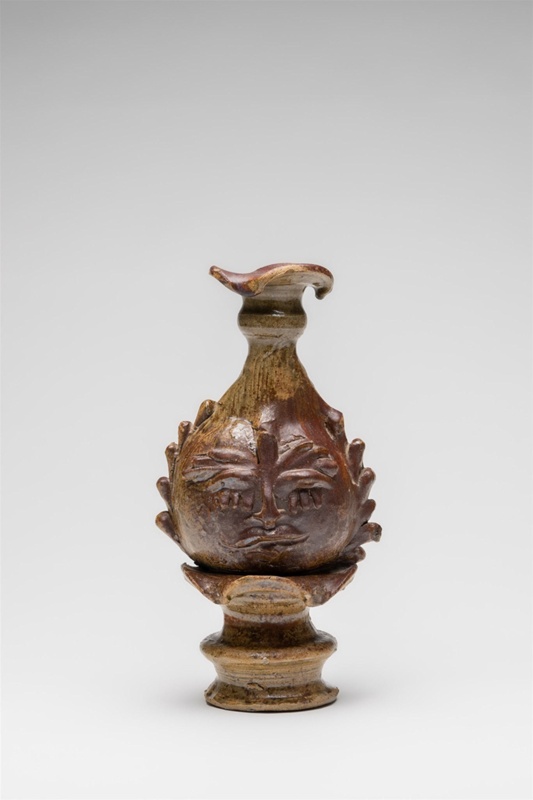 Sculptured single candlestick holder with Greenman motif featured on both sides of body. Layered detailing around elevated base.