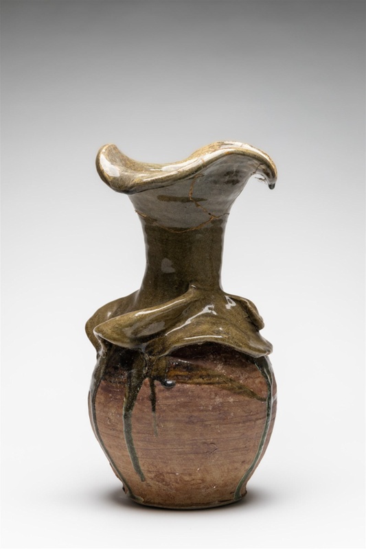 Long necked wavy lipped vase, with light olive-green glaze dripped over terracotta-brown washed glaze. A prominent Undulating wave-like design is sculptured around the shoulder of the vessel. 