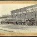 [Traction engine with four wagons loaded with wool bales outside Miles & Co Limited, Timaru]; 1895-1915; 1828