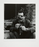 [Man in front of wooden house holding plant]; Fichter, Robert; ca. 1967; 1971:0448:0001