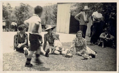 Photo, Four women sit in grass (Mavis O'Donald on right), boy in foreground; RAP2020.0165