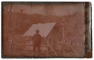Photo, Man stands before tent/hut; RAP2020.0193