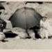 Photo, Three women with hats and umbrellas at beach, one child; RAP2020.0012