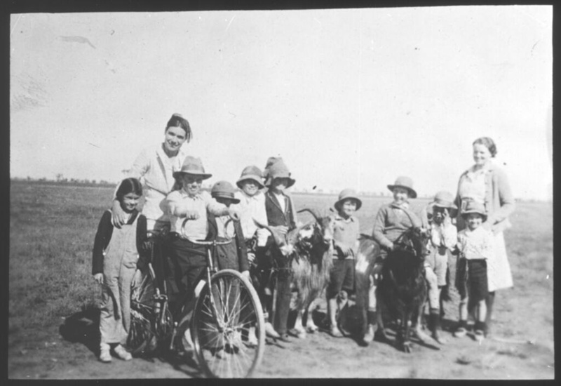 Two women and nine children, two of whom are riding goats, one of whom ...